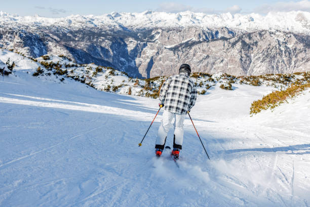 An Asian man skis down a snowy mountain in the picturesque European Alps. The scene captures the thrill and beauty of winter sports amidst a stunning alpine backdrop.