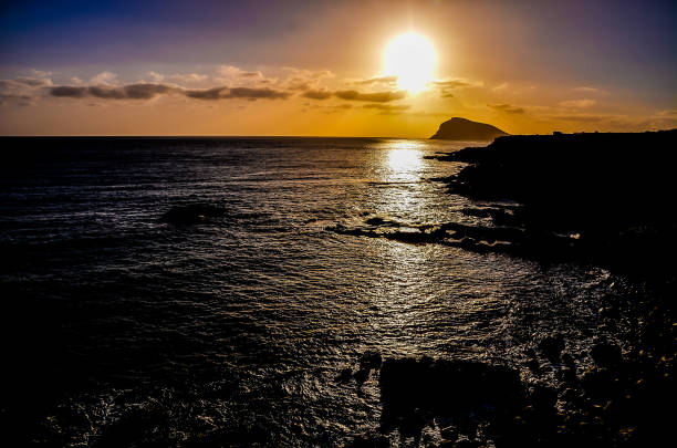 The sun is setting over the ocean, casting a warm glow on the water. The sky is a mix of blue and orange, creating a serene and peaceful atmosphere. The water is calm, with no waves or ripples