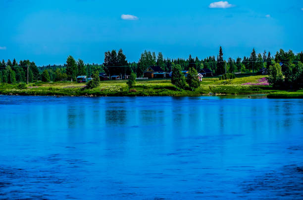 A calm lake with a blue sky and trees in the background. The water is still and the reflection of the trees can be seen in the water