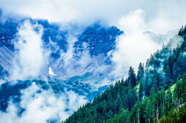 The sky is cloudy and the mountains are covered in trees. The clouds are white and fluffy, giving the scene a peaceful and serene atmosphere