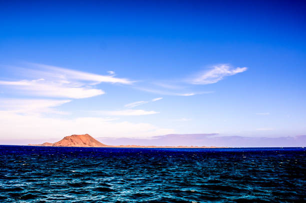 A beautiful blue ocean with a mountain in the background. The sky is clear and the sun is shining brightly