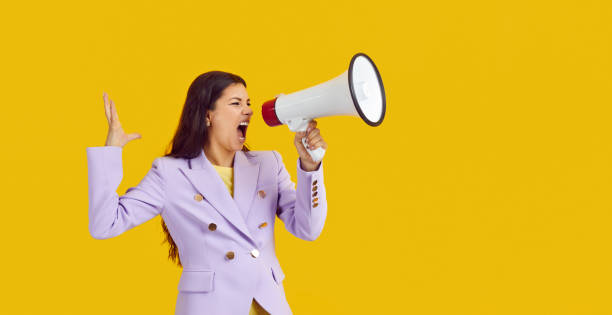 istock Emotional female activist with megaphone makes loud message on yellow background. 2193272612