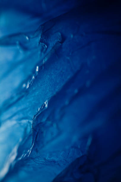 Extreme close up of blue empty plastic bag background. The plastic surface is wrinkly and tattered making abstract pattern. Selective focus, shallow depth of field.