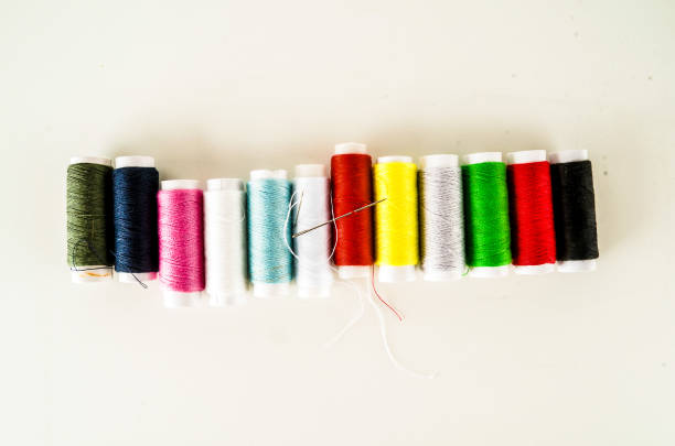 A row of colorful spools of thread are lined up on a white background. The spools are of various colors and sizes, and they are arranged in a neat row. Concept of organization and order