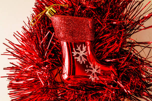 A red ornament with a snowflake design sits on a red garland. The ornament is a small red stocking or boot
