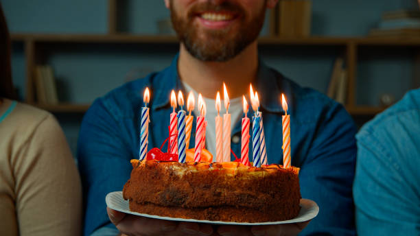 Close up festive cake with burning candles happy bearded unrecognizable birthday man smiling make wish celebrate event with friends at home party celebration anniversary year tradition congratulation
