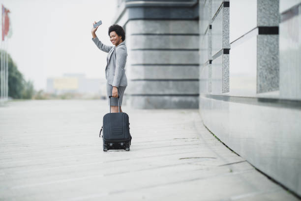 A successful black business woman greets to someone while walking with her luggage outside of the airport.