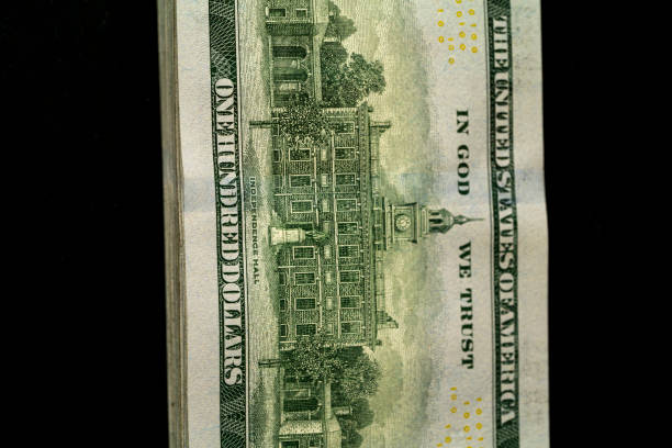 A close-up view of a one hundred dollar bill showcasing detailed historic architecture with an inscription about trust, set against a dark background.