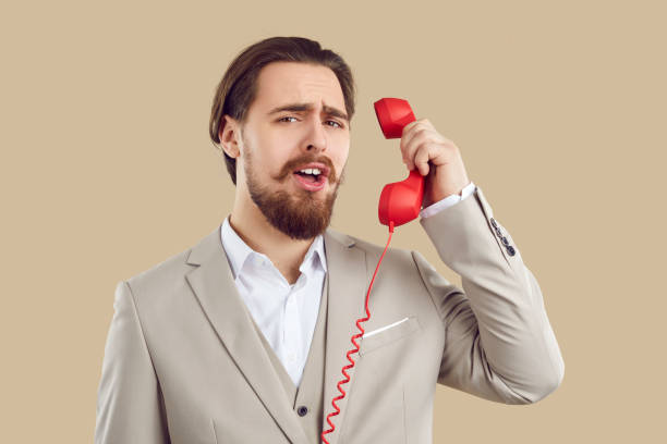 istock Amazed male client listens to information while talking on landline phone on beige background. 2193280753