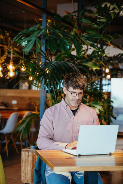 istock Serious businessman working remotely on laptop in cozy cafe environment while checking his smartphone for messages or updates on a sunny day 2193282496