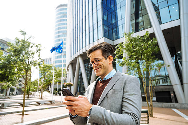 istock Smiling businessman is using smart phone for messaging near office building.Modern financial district in the city with business people 2193282553