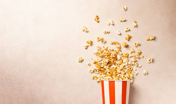 istock Popcorn explosion in red and white striped box on neutral background with copy space. Perfect for concepts related to movie nights, cinema snacks, entertainment, fun food, and party themes. 2193287163