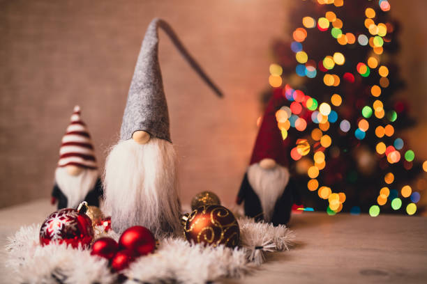 Decorative holiday gnomes surrounded by festive ornaments and white garland, placed in front of a beautiful bokeh Christmas tree, creating a charming and cozy seasonal atmosphere.