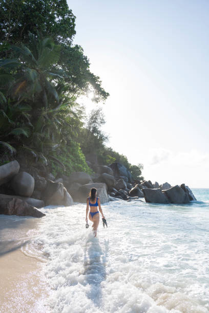 Young woman prepares to go snorkelling from rocky coastline, Seychelles