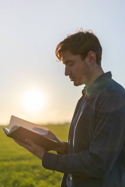 istock Young man reading a book in a field at sunset 2193297987