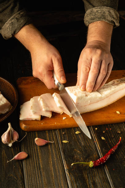 istock Hands skillfully slice through fresh pork on a wooden cutting board, surrounded by garlic cloves and a bright red chili pepper. A serene kitchen atmosphere enhances the culinary craft 2193299829