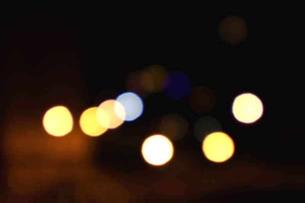 An enigmatic and dreamy depiction of blurred urban lights at night. Vibrant, colorful orbs in various shades—yellow, blue, and white—glow softly against a dark backdrop, creating a sense of warmth and intrigue. This abstract image captures the essence of city nightlife, making it ideal for artistic or atmospheric projects.