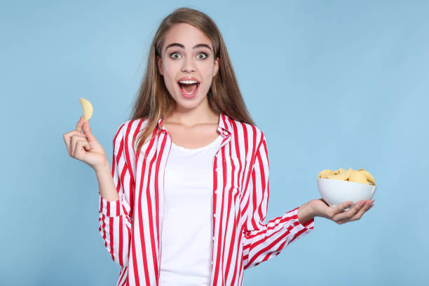 istock Young beautiful girl with potato chips in bowl on blue background 2193303005