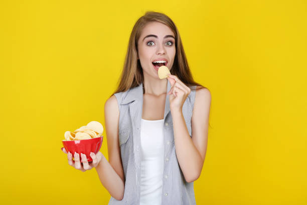 istock Young beautiful girl eating potato chips on yellow background 2193304034