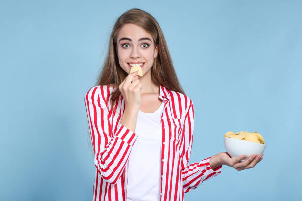 istock Young beautiful girl eating potato chips on blue background 2193304599