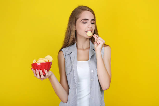 istock Young beautiful girl eating potato chips on yellow background 2193304646