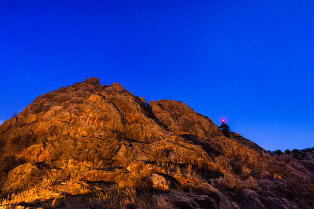 Rock Climbing at Night with Headlamp - Climber on tall rock formation up against clear sky of stars with climber going up with red headlamp.
