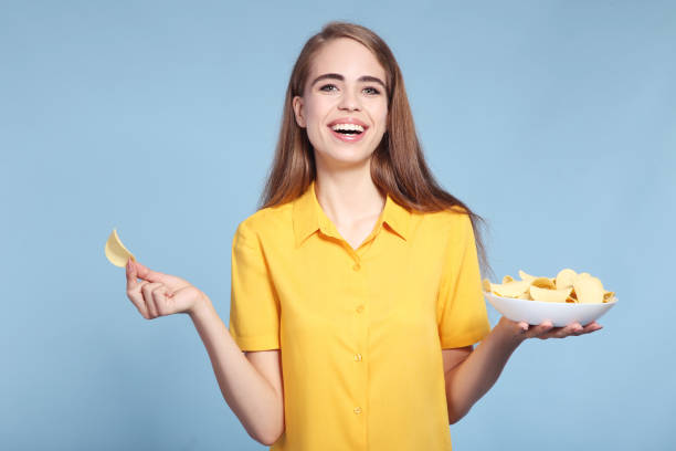 istock Young beautiful girl with potato chips in bowl on blue background 2193305316