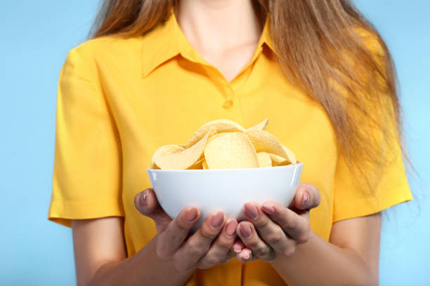 istock Young girl with potato chips in bowl on blue background 2193305452