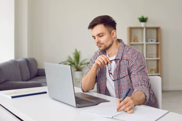 istock Concentrated young man listens to online lecture and writes information in notebook. 2193305489