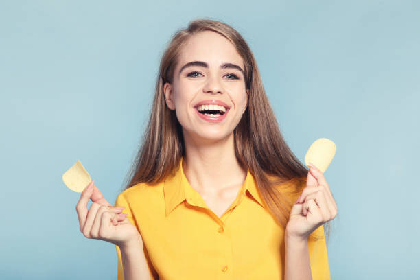 istock Young beautiful girl with potato chips on blue background 2193306275