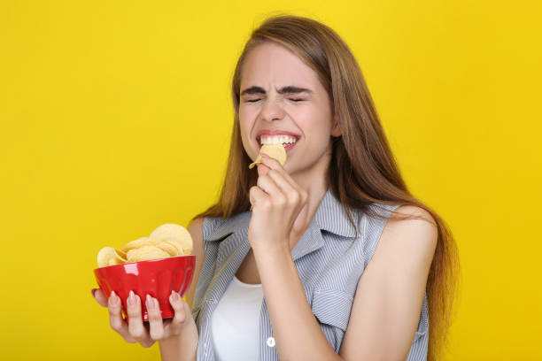 istock Young beautiful girl eating potato chips on yellow background 2193306535