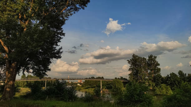 A bridge crosses a river, with trees lining the banks and a cloudy sky overhead.