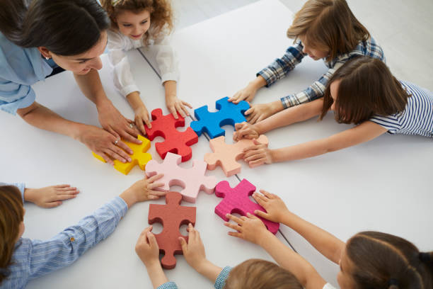 Team of creative little children with teacher put together pieces of jigsaw puzzle stock photo