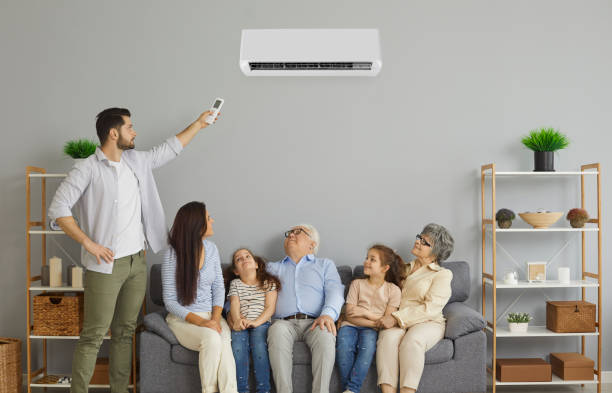 Happy family sitting on the sofa in the living room with a modern air conditioner Happy family enjoying fresh air in cozy living room interior with new air conditioner at home. Young mother, kids and grandparents together relax on comfortable sofa under AC that father has turned on air conditioner family stock pictures, royalty-free photos & images