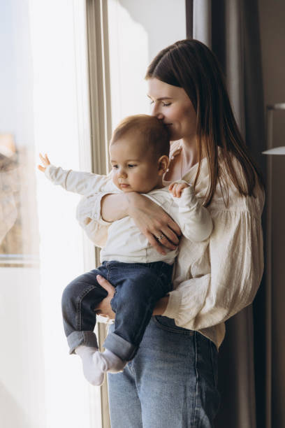 istock Mother holding her baby and looking out the window 2193316548