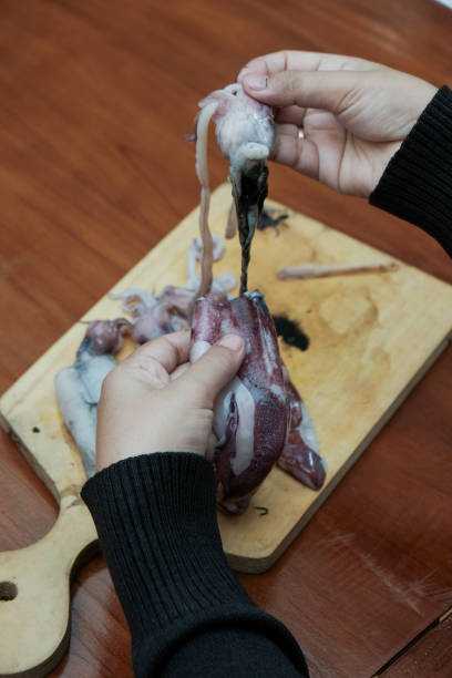 Closeup of hand Woman pulling the head squids on a cutting wooden board in the kitchen in the home