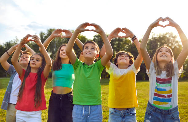 Happy children making heart shapes with their hands raised Happy children making heart shapes with their hands raised. Group of smiling boys and girls playing on nature outdoors in sunny day. Kids joining hands in shape of hearts expressing love cute boy show love symbol hand stock pictures, royalty-free photos & images