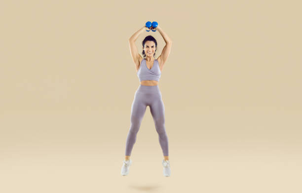 istock Smiling woman doing sport workout bouncing with dumbbells isolated on light beige background. 2193326951