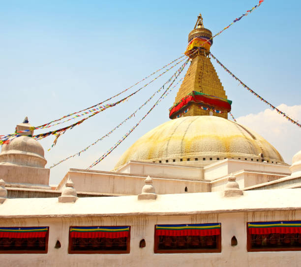 The prominent Boudhanath Stupa in Kathmandu, Nepal is depicted with vibrant prayer flags against a bright clear blue sky. A spiritual and iconic landmark of rich Buddhist culture and heritage.