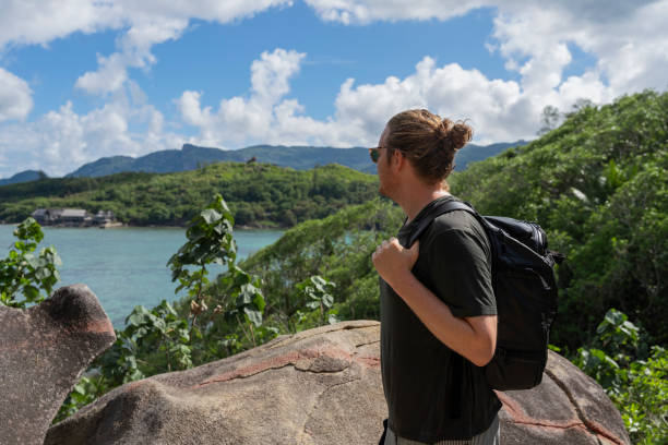 Young man hiker stands on top of island above jungle and sea,  Moyenne Island, Seychelles