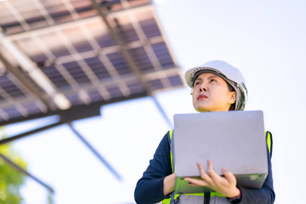 istock A female technician in a hard hat and reflective vest conducts a solar panel inspection with a laptop and a handheld device under a solar carport structure. The panels and sunlight frame the scene. 2193347304