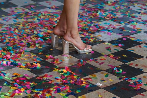 istock Feet in heels standing in rainbow colored confetti on black and white checkered floor 2193352028