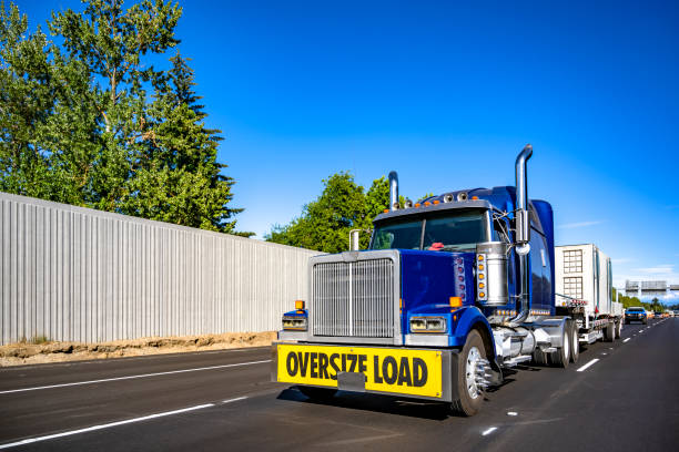 istock Bright blue big rig semi truck with oversize load sigh on the front bumper transporting oversized cargo on step deck semi trailer driving on the straight highway road at sunny day 2193352734