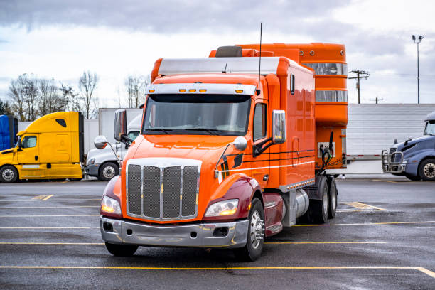 istock Orange big rig semi truck with extended cab transporting cargo in dry van semi trailer running to exit from truck stop parking lot 2193353238