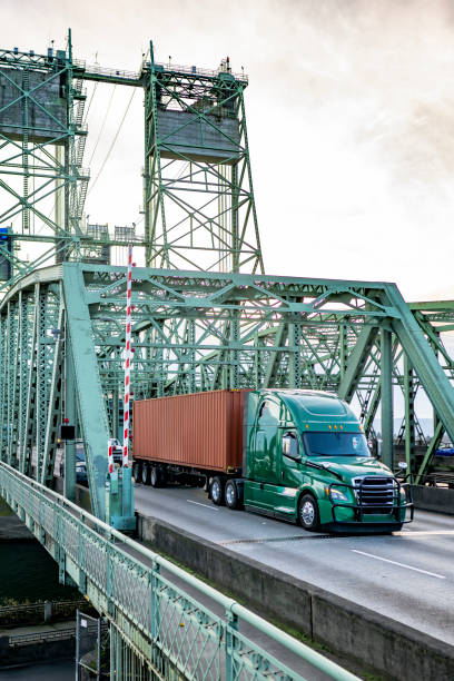 istock Powerful green big rig semi truck with high cab and grille guard transporting container on semi trailer running on the truss Columbia River Interstate bridge 2193353254