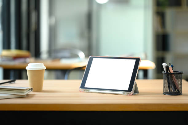 Digital tablet with empty screen, coffee cup and pencil holder on wooden office desk.