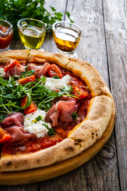 istock Pizza prosciutto - cured ham, white mushrooms, arugula and cheese on wooden table 2193364919