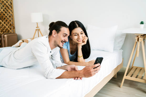 istock A couple enjoys quality time together, sharing smiles while looking at a smartphone in a cozy bedroom setting. 2193374625