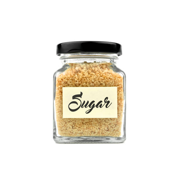 istock Brown sugar in a glass bottle isolated on white background. Granulated sugar, with word SUGAR on yellow stick note paper and black lid. Modern and stylish. Close up. 2193376549