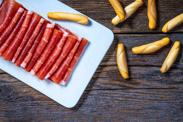 Ham serrano tapas from Spain, Iberian ham from Spanish tapas folded in a row on a dark wood background board.